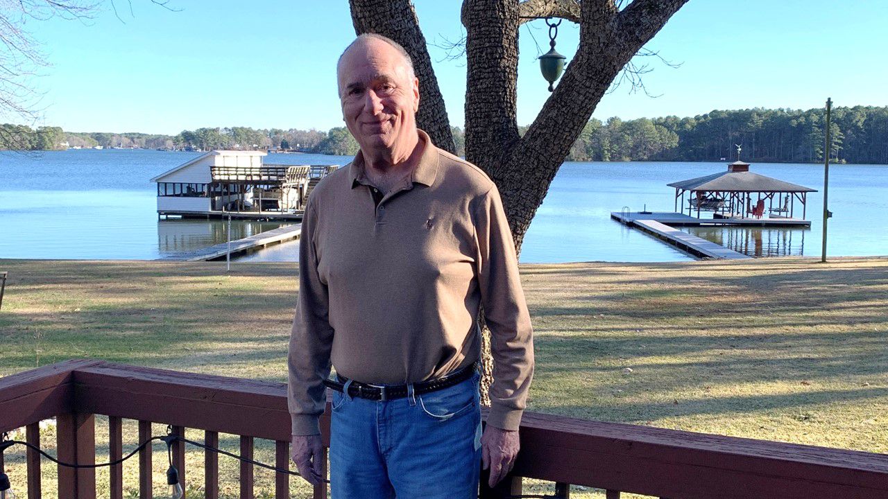 Older man standing on deck with lake in the background